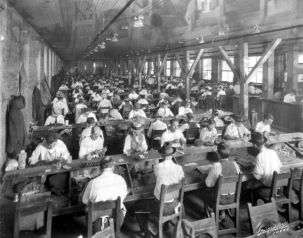 Black and white photo of workers seated at tables and rolling cigars.